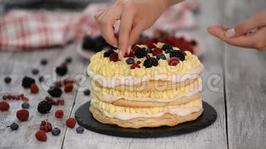 糖果女孩把夏天的浆果放在奶油层蛋糕上。 女人准备一个奶油和浆果蛋糕。