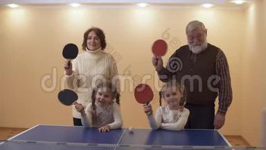 爷爷奶奶站在网球场附近，两个小孙女挥舞着球拍，然后挥动着手