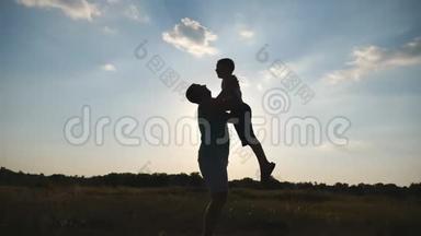 快乐的爸爸把他的小男孩扔到空中向大自然。 父亲和儿子在草地上玩耍的剪影