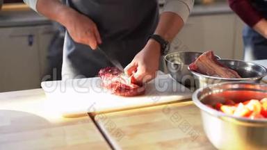 穿灰色围裙的厨师在塑料板上切肉。 烹饪过程的特写照片