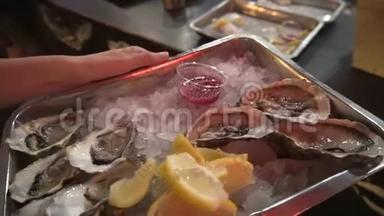 一个年轻的美食家手里拿着冰、柠檬和酱汁，在托盘上品尝新鲜牡蛎。