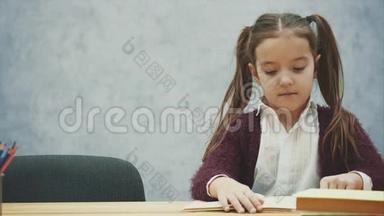 小女孩读一本书坐在灰色<strong>的</strong>内部。 学习教科书<strong>的</strong>女<strong>学生</strong>。 <strong>穿校服的</strong>孩子