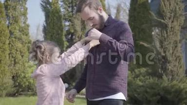 小女孩试图扣父亲站在户外的衬衫。 家庭休闲户外，春天，聚会