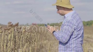 英俊的农民与智能手机站在田间向日葵与<strong>联合</strong>收割机的背景。 现代概念