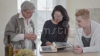 一位留着长发的老年妇女向朋友们<strong>展示</strong>她的旧<strong>相册</strong>。 三个中年成熟妇女组