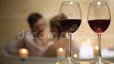 红葡萄酒杯站在心爱夫妇的背景下，在浴缸里享受着