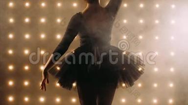 穿着黑色芭蕾舞裙的芭蕾舞演员剪影正在黑暗的工作室里跳芭蕾。