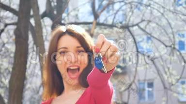年轻兴奋的女孩带着蓝色钥匙链展示新房地产的钥匙，女手拿着红色指甲拿着钥匙
