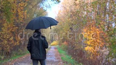 一个身材苗条的男人，头发灰白，戴着眼镜，穿着一件<strong>黑色夹克</strong>，手里拿着一把<strong>黑色</strong>雨伞，走在里面
