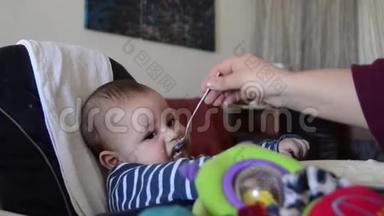 可爱的六个月大的小男孩试图接触玩具，而妈妈正在喂他