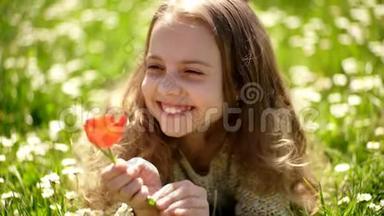 女孩躺在草地上，草地在背景上。 郁金香香的概念.. 笑脸上的女孩捧着红色的郁金香花