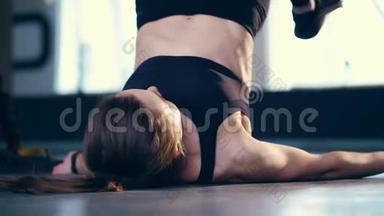 漂亮的金发女郎穿着黑色<strong>紧身</strong>裤、<strong>上衣</strong>和运动鞋，躺在地板上练习TRX环、支架