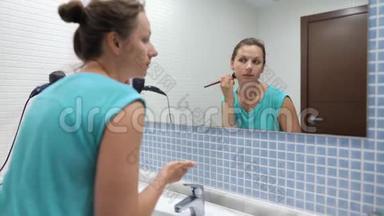 漂亮的女人在浴室镜子前用化妆刷粉脸