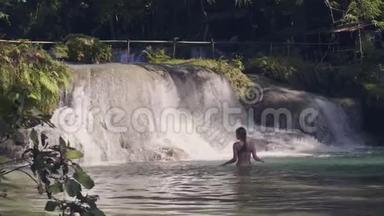年轻女子在热带森林的瀑布里洗澡，<strong>溪水</strong>溅在背景上。 流动水浇注量