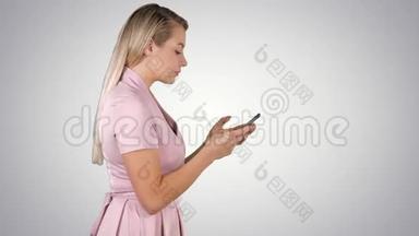 穿粉色连衣裙的漂亮女人在渐变背景下用智能手机发短信。