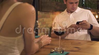 年轻人在晚上的咖啡馆里用<strong>手机</strong>浪漫<strong>约会</strong>。 帅哥在浪漫的餐桌上看智能<strong>手机</strong>