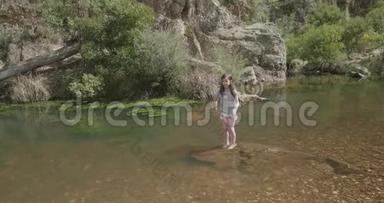 年轻女孩脚踝深深地站在河中的岩石上，然后上下跳动