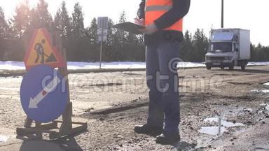 一名男工程师在一个坏路标的背景下检查路面和路面坑的质量
