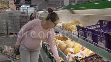 在超市里戴眼镜的年轻孕妇选择新鲜的有机水果。 女人在购物时选择水果。