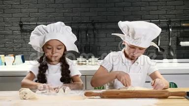 可爱的学龄前儿童在私人厨房里扮演真正的厨师。 穿白色围裙和厨师帽的儿童使用擀面杖