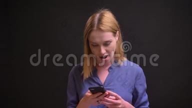 白种人金发女人穿着衬衫观看智能手机的肖像，黑色背景下<strong>有</strong>积极的<strong>惊喜</strong>。