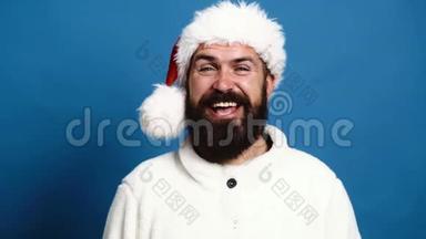 戴着`顶帽子的大胡子男人在蓝色的背景上真诚地微笑。 蓝色背景的搞笑圣诞老人。 概念
