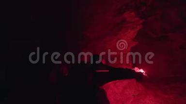 人走在神秘的地下洞穴里，黑暗的墙壁背景上有一个红色的燃烧信号耀斑。 库存数据