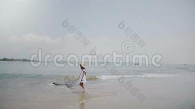 大气背景拍摄的快乐小女孩在异国情调的海洋海滩上漫步，戴着大草帽。