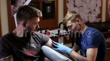 一个专业的纹身艺术家在纹身店`男人的手臂上做纹身。