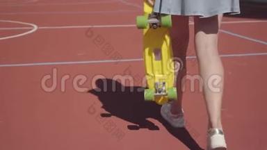 腿的女人穿着短裙，带着黄色滑板在篮球场上行走。 穿运动鞋的女人腿