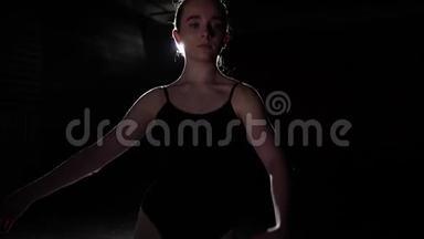 肖像可爱的芭蕾舞演员站在聚光灯下的黑色背景在工作室。 芭蕾舞表演经典芭蕾舞表演