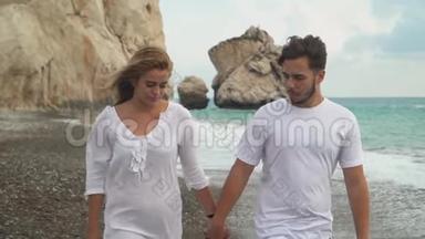 一对穿着白色衣服的年轻夫妇在海边或海边的岩石海岸散步，彼此拥抱着交流