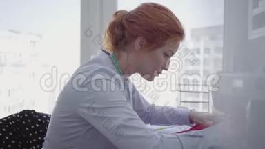 专<strong>业</strong>成功的红发女人在车间的桌子上缝纫。 裁缝工作<strong>勤奋</strong>，细心. 霍比特人
