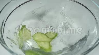 慢动作，几片鲜黄瓜片<strong>落入水中</strong>.. 把绿色黄瓜切在一个白色的玻璃碗里