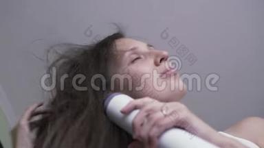 那个女孩用吹风机吹干头发。 一个没有化妆的年轻女孩用吹风机擦干头发。 早上的造型。