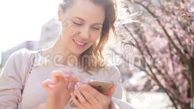 成熟的女人手里拿着智能手机，微笑着。 玉兰盛开在城市街道上，春天的肖像
