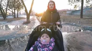早春，妈妈带着一个婴儿车在<strong>公园里散步</strong>，在冰雪融化的水坑间<strong>散步</strong>。