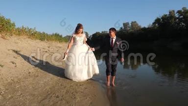 美丽的新娘穿着白色的裙子，新郎赤脚在河岸边的水中行走。 相亲相爱的一对