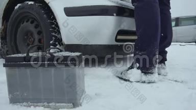 人们在冬天降雪时修理或修理破车。 汽车故障或问题。 汽车电池就在旁边
