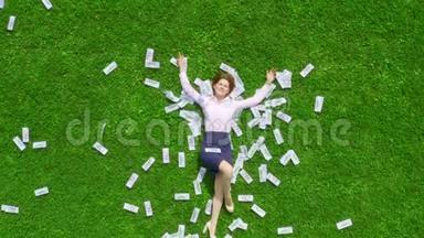 年轻漂亮而成功的女商人躺在一片绿草丛生的草坪上，草坪上<strong>到处都是</strong>钱。