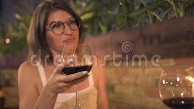 微笑的女人手里拿着红酒杯，在晚上的晚餐上说话。 快乐的女人喝红酒浪漫
