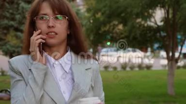 女人在智能手机<strong>上</strong>说话，在公园里喝咖啡。 戴眼镜的女商人穿着轻便西装<strong>上</strong>班