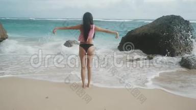 穿着泳装、双臂张开的苗条女孩站在海滩上，看着海浪，<strong>稳重</strong>