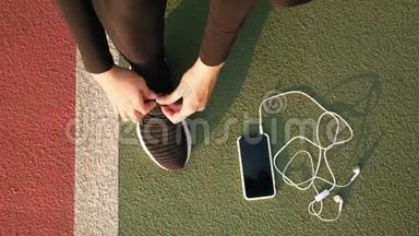 女跑步者的脚准备把运动鞋和耳机绑在地上。 关门