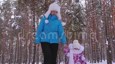保姆在雪地路上牵着小女孩的手，冬天在公园里清新的空气中散步。 妈妈和女儿先做