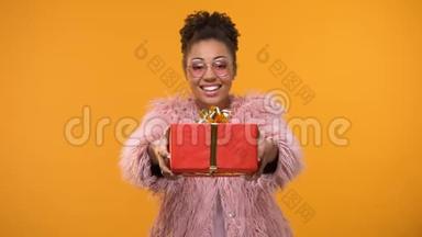 微笑的美国女人伸出双手展示礼品盒，明亮的背景