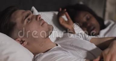 多民族夫妇躺在床上。 男人在床上遭受伴侣的鼾声。 夫妻生活方式和人