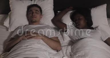 多民族夫妇躺在床上。 男人在床上遭受伴侣的鼾声。 夫妻生活方式和人
