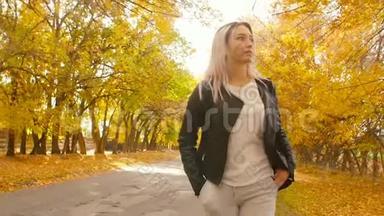 年轻漂亮的女孩走在秋天的跑道上，一个穿着皮<strong>夹克</strong>和<strong>运动</strong>服的年轻时髦女人走在沥青路上