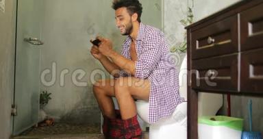 男人坐在马桶上用手机智能手机年轻的拉丁男人玩游戏